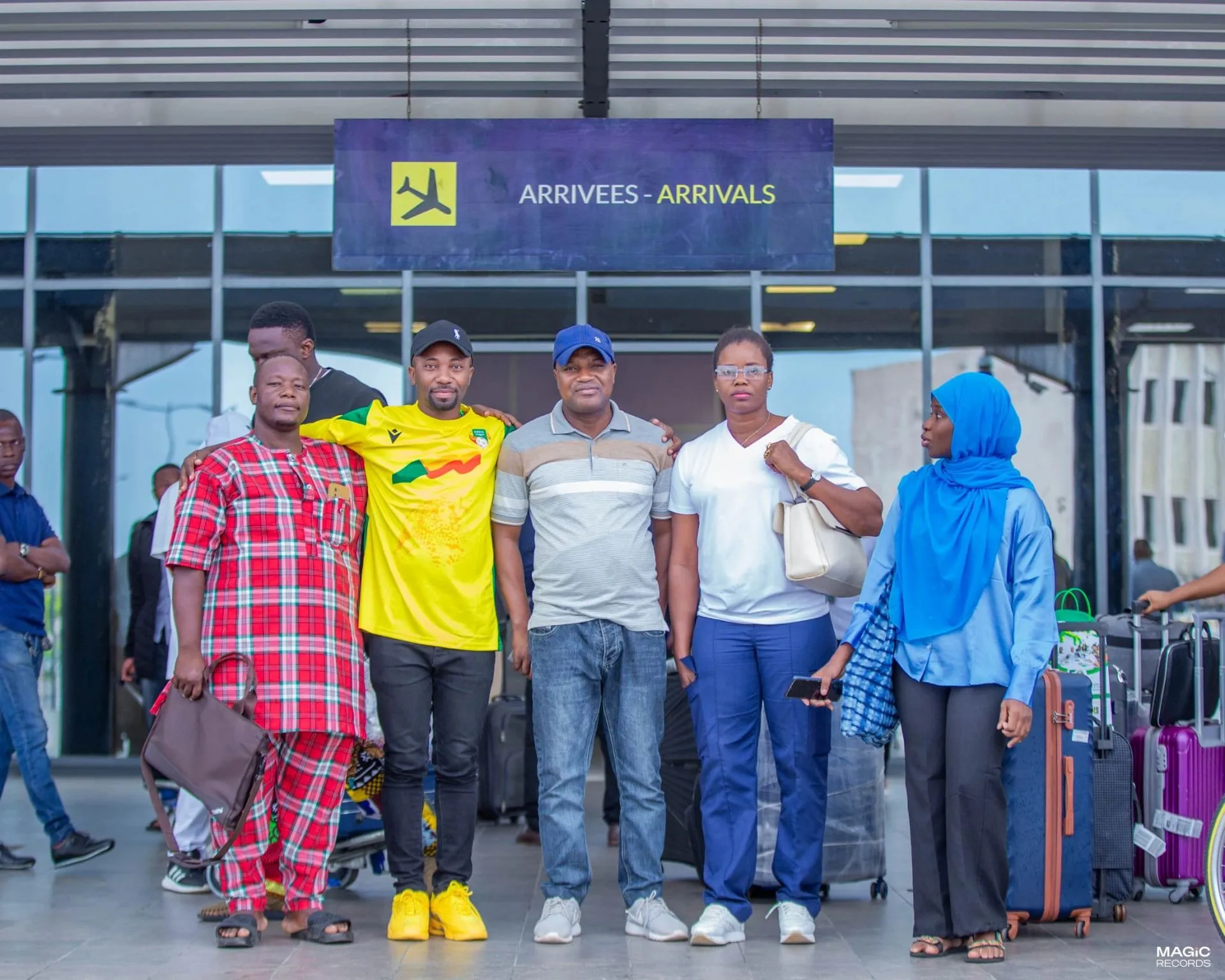 Des personnes brandissent des maillots aux couleurs nationales dans un hall d'aéroport.
